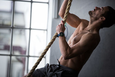 Full length of shirtless climbing a rope 