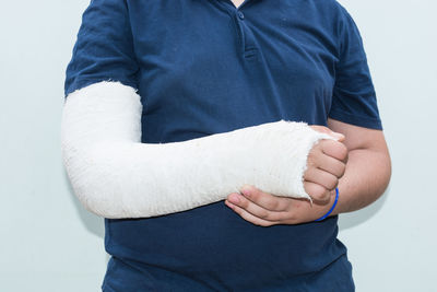 Midsection of man with broken arm standing against white wall