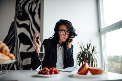 Woman in blazer having wine while reading magazine at table