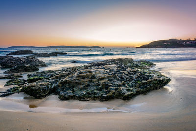 Rocks on shore at beach during sunset