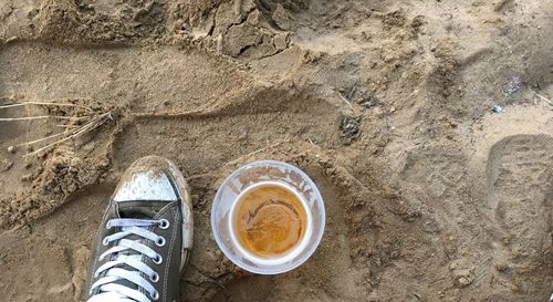 Low section of person by beer glass on sand at beach