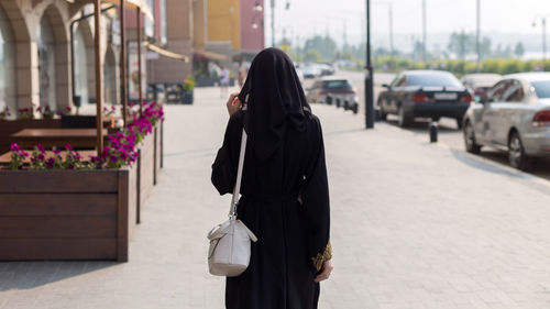 A single muslim woman walks through an empty big city, rear view.