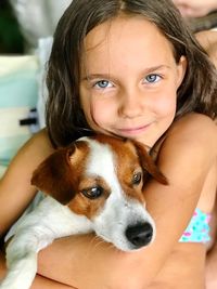 Portrait of cute girl embracing dog at home