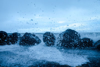 Close-up of wet glass against sky