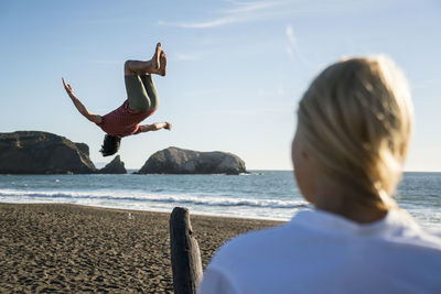 Teenage boy back flipping off see-saw on beach