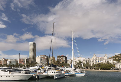 Boats moored at harbor against cloudy sky