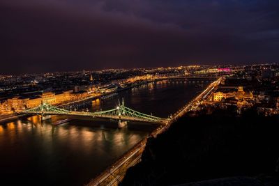 Illuminated bridge over river in city at night