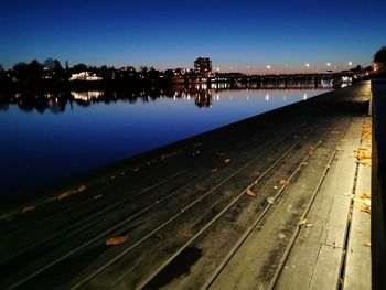 Illuminated city by river against clear sky at night