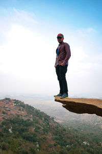 Portrait of man standing on rock formation against sky