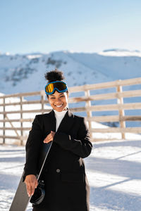 African american woman with goggles and a snowboard on a snowy mountain during winter