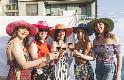 Portrait of smiling female friends toasting drinks while standing outdoors