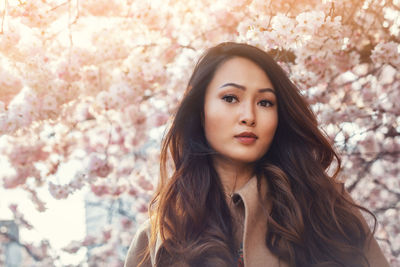 Young asian woman, in front of blossoming cherry tree in the spring time