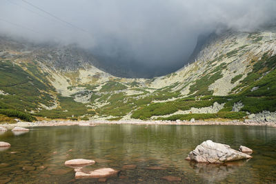 Scenic view of lake by mountains against cloudy sky