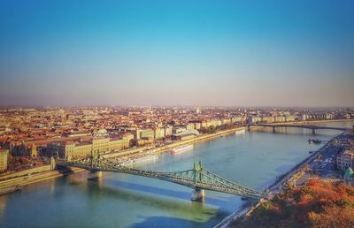 Bridge over river in city against clear blue sky