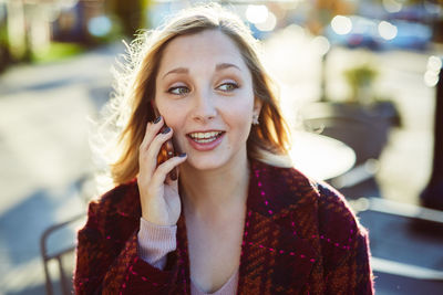 Young woman talking on mobile phone while sitting at sidewalk cafe