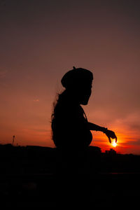 Silhouette woman standing against orange sky