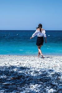 Rear view of young woman walking on beach against clear sky