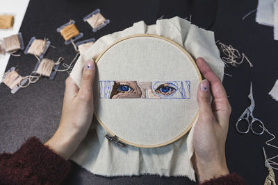 Hands of young woman holding embroidery frame on table in studio