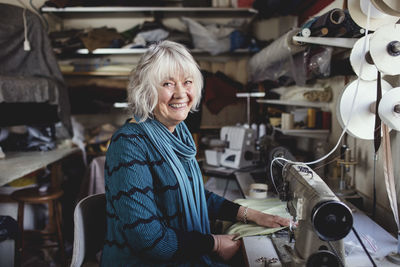 Portrait of smiling senior owner sitting at sewing machine in workshop