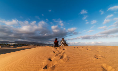 Rear view of women on sand dune in desert against sky