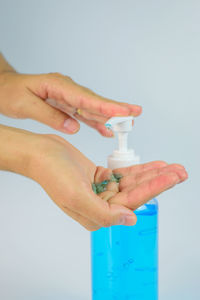 Close-up of hand holding bottle against gray background