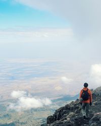 Rear view of man walking on cliff against cloudy sky