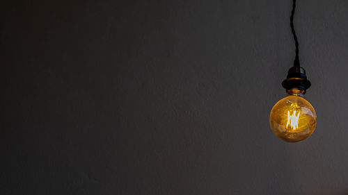 Close-up of illuminated light bulb hanging from ceiling