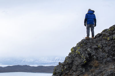 Rear view of man standing on rock against sky