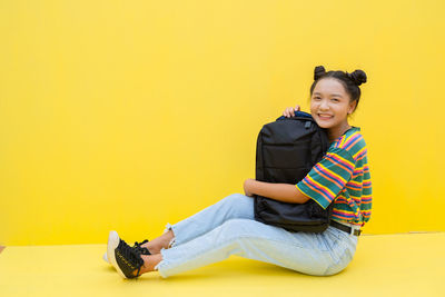 Portrait of smiling girl sitting on yellow background