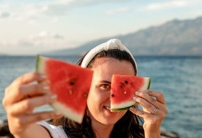 Portrait of happy young woman holding piece of watermelon in front of face.