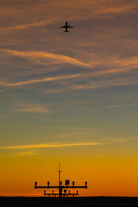 Low angle view of silhouette airplane flying against sky during sunset