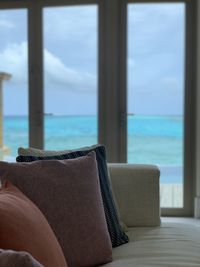 Chair by sea against sky seen through window