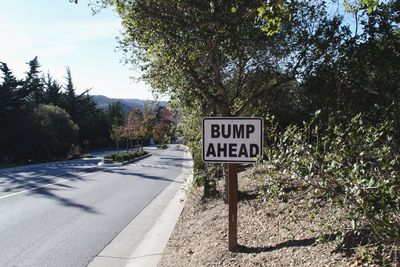 Road sign by trees against sky, bump ahead, meta