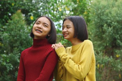 Happy teenage friends smiling against trees