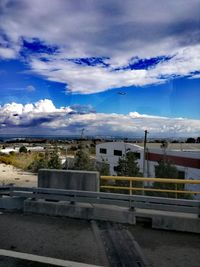 Empty road along built structures and clouds