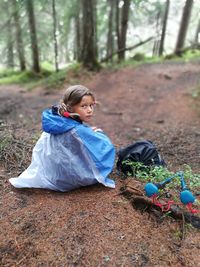 Rear view of girl wearing raincoat sitting on field in forest
