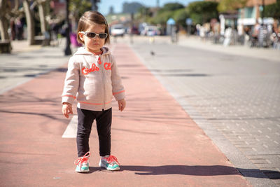 Portrait of girl wearing sunglasses while standing on footpath in city