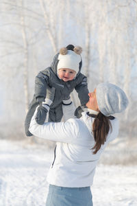 Smiling mother standing with daughter on snow covered land