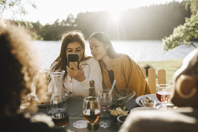 Young woman using smart phone while sitting with female friends at party