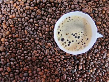 Directly above shot of roasted coffee beans with coffee cup