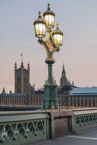 Illuminated street light in city against sky