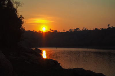 Silhouette trees by lake against sky during sunset
