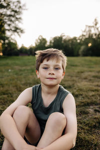 Portrait of boy sitting on grass in playground