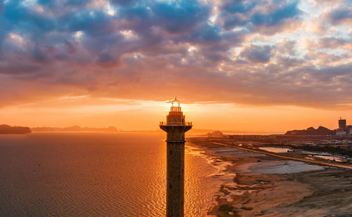 Lighthouse at beach against sky during sunset