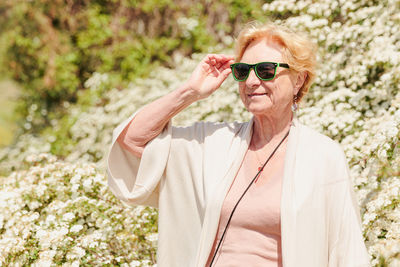 Elderly woman posing among bushes with white flowers