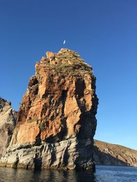 Rock formation by sea against clear blue sky