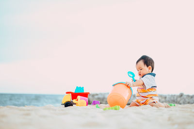 Boy sitting on toy at beach against sky