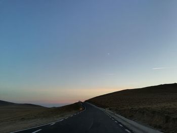 Road passing through landscape against clear blue sky