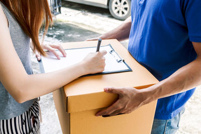 Midsection of woman signing paper while delivery person holds package