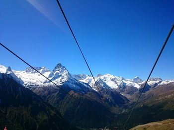 Overhead cable car over snowcapped mountains against blue sky